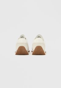 Λευκά δερμάτινα αθλητικά παπούτσια με ανάγλυφη επάνω επιφάνεια, καφέ λαστιχένια σόλα με ζιγκ-ζαγκ σχέδιο, στρογγυλεμένη φτέρνα και μινιμαλιστικό σχεδιασμό.