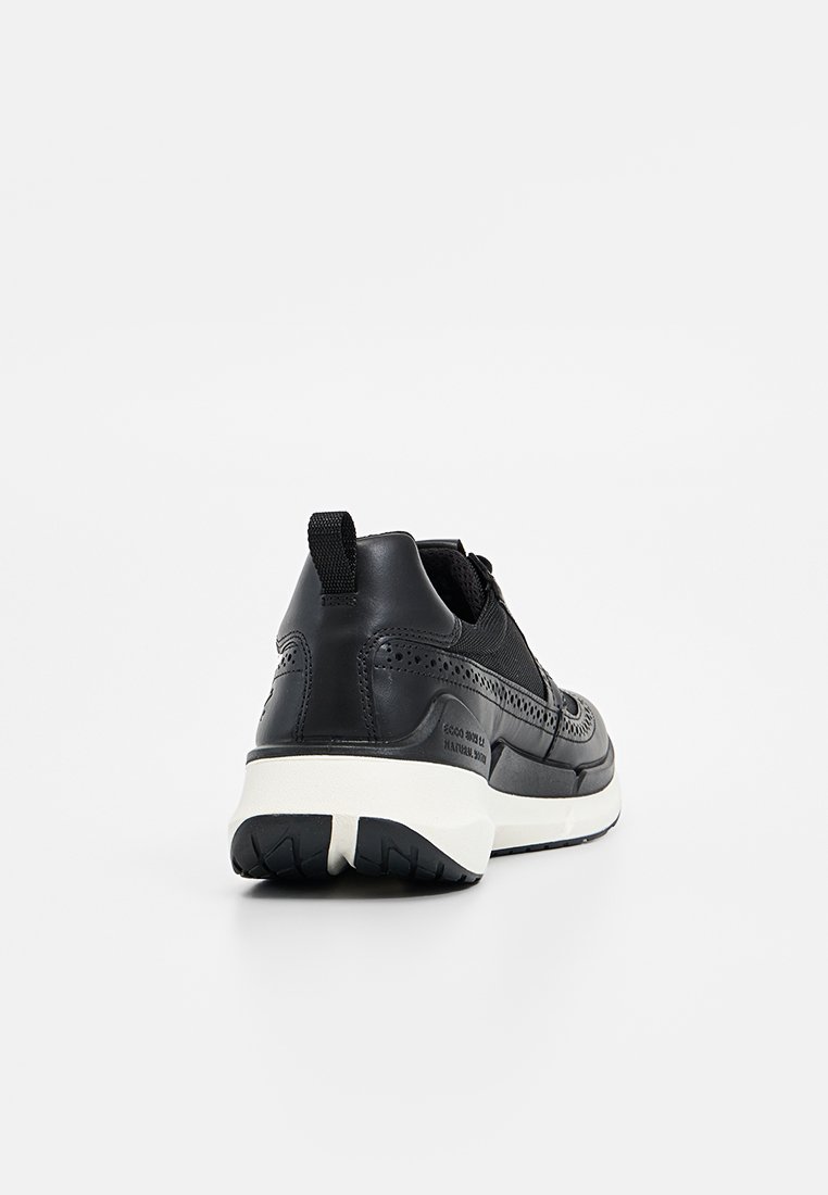 Baskets noires avec une tige en cuir lisse, des accents en mesh, une épaisse semelle blanche et des détails de perforation subtils au niveau du talon et des côtés.