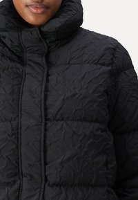 Black puffer jacket with a high collar, featuring a quilted pattern, textured fabric, and a full zipper closure along the front.