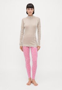 Lys beige langermet topp med teksturerte mønstre og tommelhull, kombinert med rosa leggins med geometrisk snøflakdesign.