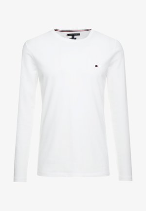 Camiseta de algodón blanca de manga larga con cuello redondo y un pequeño logo en el pecho, con acentos de rayas rojas y azules en el cuello.