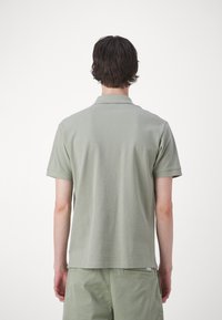 Polo tričko s krátkym rukávom v tlmenej zelenej farbe, vyrobené z jemnej bavlny, s klasickým golierom a lemovaním, skombinované so svetlozelenými šortkami.