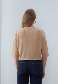 Bronzefarbenes, geripptes Crop-Top mit kurzen Ärmeln und rundem Ausschnitt. Trägt man mit dunkelblauen High-Waist-Jeans, von hinten gezeigt.