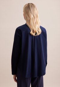 Marineblauwe lange mouw shirt met een licht gebogen zoom, rug yoke detail en knopenmanchetten. Zachte, gladde stoftextuur.