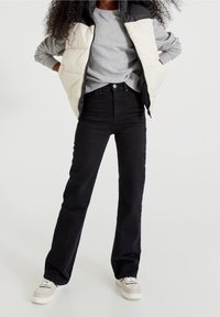 Puchowy kamizelka w czarno-kremowe panele na szarej bluzie, zestawiona z czarnymi jeansami o wysokim stanie i białymi sneakersami z beżowymi akcentami.