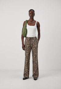 Buks med leopardmønster og vide ben, med elastisk liv, sammen med en hvit ribbestrikket tanktopp og en teksturert grønn skulderveske.