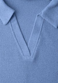 Detailní záběr světle modré žebrované pleteniny s výstřihem do V a přeloženými klopami na oděvu.