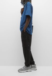 Blaues übergroßes T-Shirt, schwarze Cargo-Hosen mit Taschen und graue Sportschuhe mit Netzakzenten. Textilstruktur für Komfort.