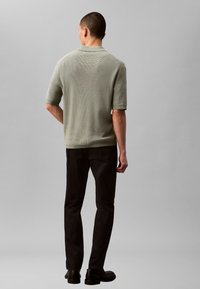 Tricou polo verde deschis cu textură tricotată, cu mâneci scurte, asortat cu pantaloni negri și pantofi negri. Cusături și detalii la guler vizibile.