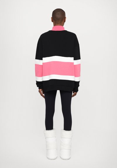 Hanorac supradimensionat de culoare neagră și roz, cu dungi albe și roz, asortat cu colanți negri și cizme albe căptușite cu blană.