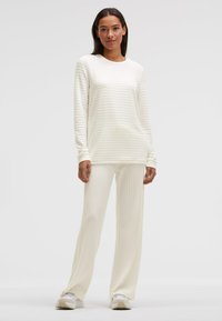 Weißes, geripptes Langarm-Oberteil und passende Hose, mit lockerem Schnitt und strukturierter Stoffstruktur. Kombiniert mit hellen Turnschuhen.