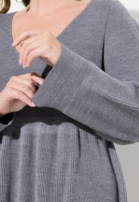 Haut en tricot gris à côtes avec un décolleté en V et de longues manches évasées, présentant une texture douce et un détail froncé à la taille.