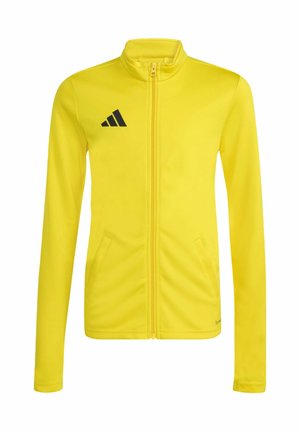 Żółta sportowa kurtka z pełnym zamkiem błyskawicznym, długimi rękawami, wysokim kołnierzem, bocznymi kieszeniami oraz czarnym logo Adidas na lewej piersi.