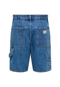 Short en denim bleu avec de grandes poches arrière, une boucle à outils sur le côté gauche, et un petit écusson de marque sur la poche droite.
