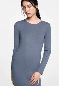 Žebrované modré šaty s dlouhým rukávem a kulatým výstřihem. Měkká textura, upnutý silueta a minimální detaily zvýrazňují jejich jednoduchost.