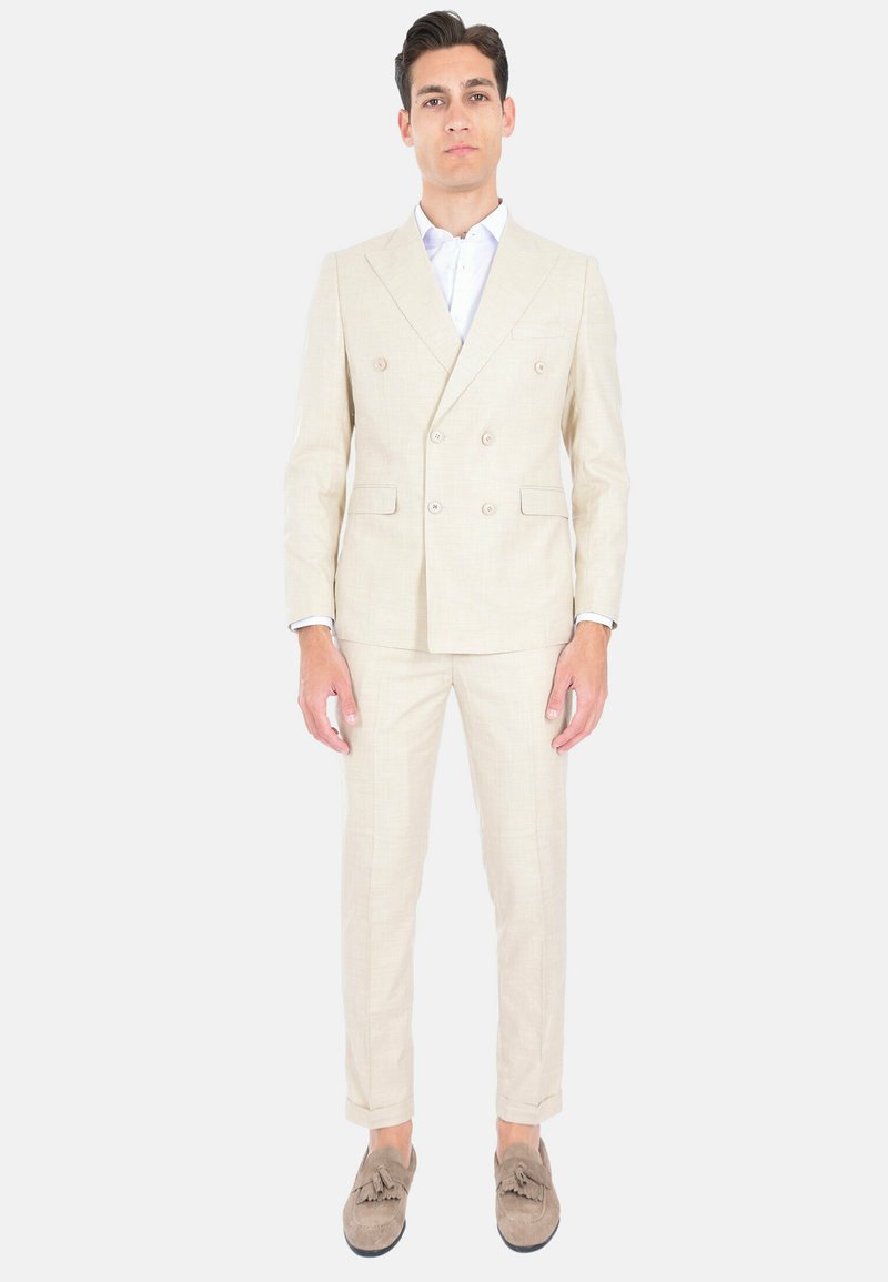 Giacca beige doppiopetto realizzata in tessuto leggero con un delicato motivo a quadri. Presenta rever a punta e pantaloni slim-fit, abbinati a mocassini color nocciola.