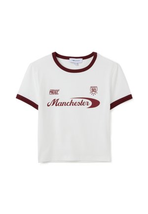 Camiseta de manga corta blanca con detalles en color burdeos, que presenta el texto "Manchester" y diseños gráficos, fabricada en algodón. Estilo de cuello redondo.