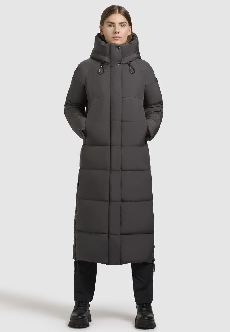 Lungo cappotto grigio imbottito con colletto alto, sezioni imbottite, tasche laterali e coulisse regolabili. Caratterizzato da un design elegante e minimal.