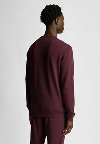 Felpa bordeaux con maniche lunghe, polsini a costine e scollo rotondo. Tessuto liscio e vestibilità comoda, abbinata a pantaloni coordinati.