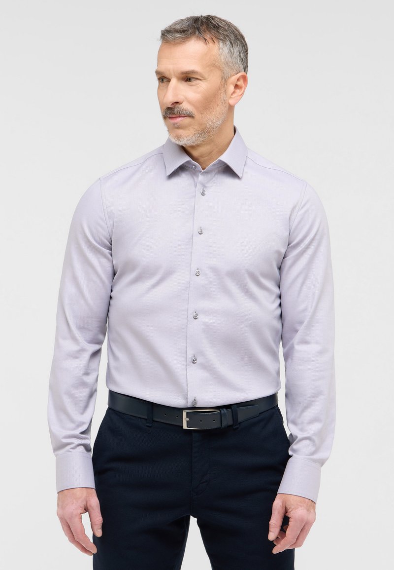 Camicia a maniche lunghe di un delicato colore viola con colletto button-down, caratterizzata da una sottile texture e cinque bottoni sulla parte anteriore, abbinata a pantaloni scuri.