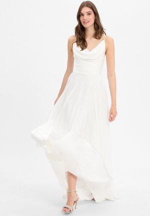 White long dress with a cowl neckline, fitted bodice, and flowy skirt. Features thin straps and drapes softly. Paired with silver-heeled sandals.