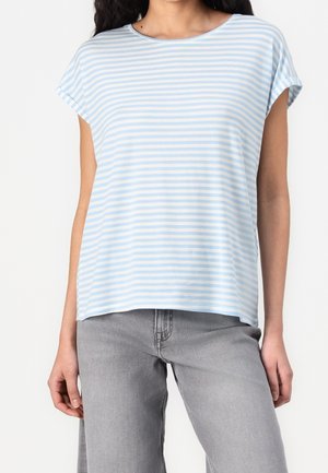 Femme portant un haut à manches courtes à rayures horizontales bleu clair et blanches, associé à un jean gris clair, debout devant un fond uni.