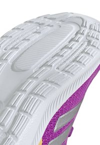 Podeszwa buta z teksturowanej białej gumy z głębokimi rowkami, przechodząca do fioletowej siateczki z srebrnymi akcentami.