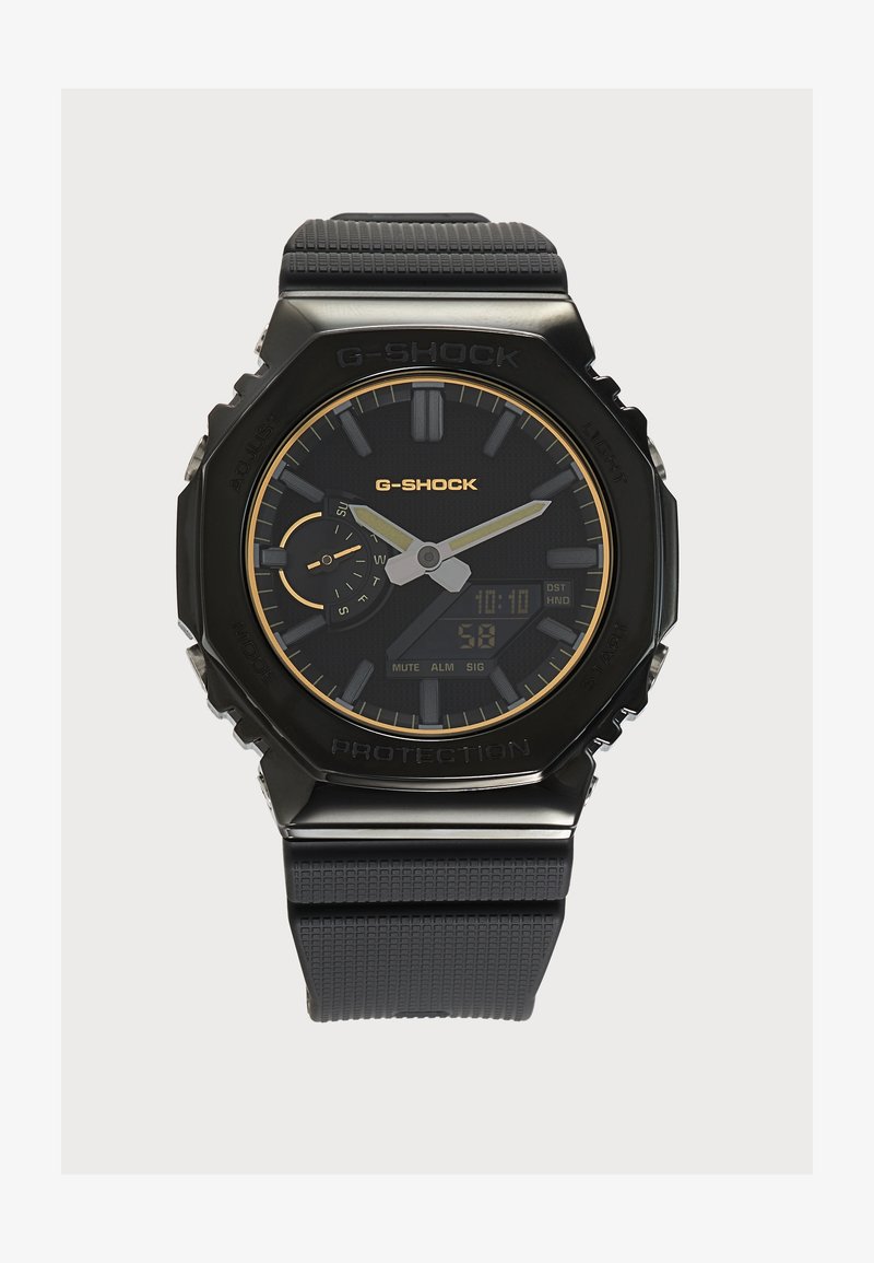 Черен ръчен часовник G-Shock с аналогови стрелки, дигитален дисплей, черна гумена каишка и златисти акценти на циферблата и името на марката.