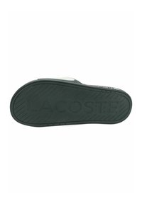 Suela de goma negra con surcos texturizados y "LACOSTE" en relieve. Tacón ligeramente elevado con un lado liso.