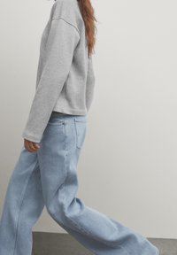 Sweat-shirt gris à coupe décontractée et manches longues, associé à un jean large bleu clair avec poches avant et une silhouette décontractée.
