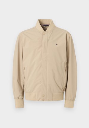 Világos bézs színű bomber dzseki, könnyű anyagból. Álló gallérral, két oldalzsebbel és bordázott mandzsettával rendelkezik, a mellkason kis logóval.