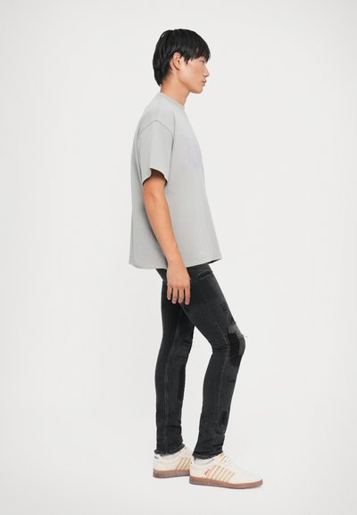 T-shirt grigia in cotone a maniche corte, abbinata a jeans skinny neri strappati e sneakers color crema con accenti arancioni e blu.