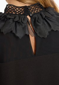 Robe noire avec un col froncé texturé, des détails en dentelle élégants avec deux boutons noirs, et une ouverture en forme de clé à l'arrière.