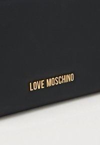 Μαύρη δερμάτινη τσάντα με υφή στην επιφάνεια και χρυσή πλακέτα με το λογότυπο "LOVE MOSCHINO." Συμπαγές σχέδιο με καθαρές άκρες.