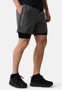 Grijze sportshorts van lichtgewicht materiaal met een logo aan de zijkant. Draag ze over zwarte compressie-shorts, gecombineerd met zwarte sneakers.