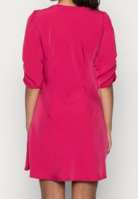 Kort rosa klänning med puffärmar, slät tyg, figurnära design och en lätt utsvängd kjol. Sömmar framhäver formen.