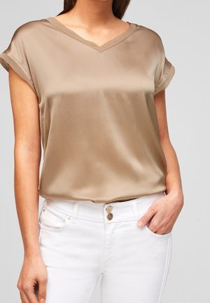 Beige satinbluse med V-hals og korte opsmøgede ærmer, kombineret med hvide jeans med dobbelt knaplukning. Glat tekstur og afslappet pasform.