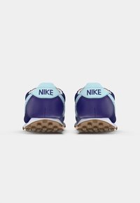 Um par de sapatilhas Nike azuis e azul claro, vistas de trás, com solas marrons texturizadas visíveis sobre um fundo branco.