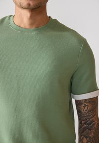 T-shirt court à manches courtes de couleur vert clair texturé avec un motif à côtes et une finition blanche contrastante au niveau des manches.