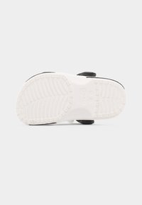 Σόλα από μαύρο και λευκό παπούτσι Crocs που δείχνει λεπτομερή μοτίβο πέλματος και κυκλικό λογότυπο Crocs στο κέντρο.