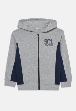 Hoodie zippé en coton gris avec des panneaux latéraux bleu marine, un logo sur le devant et une capuche avec cordon de serrage. Texture douce, coupe régulière.