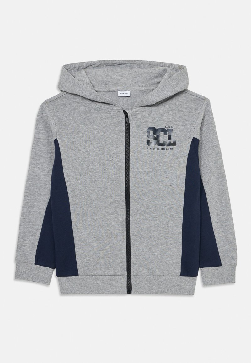 Felpa grigia in cotone con zip, pannelli laterali blu navy, logo frontale e cappuccio con cordoncino. Texture morbida, vestibilità normale.
