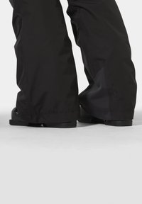 Zwarte waterdichte sneeuwbroek met een ontspannen pasvorm, voorzien van een gladde textuur, brede pijpen en subtiele merkvermelding nabij de zoom.