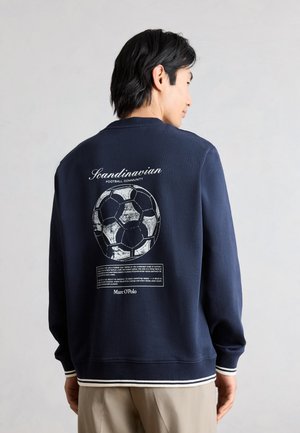 Uomo che indossa una felpa blu navy con testo bianco "Comunità calcistica scandinava", una grande grafica vintage di un pallone da calcio e un testo più piccolo sul retro.
