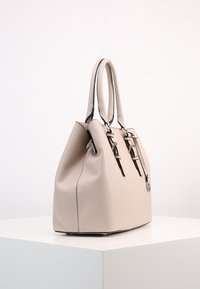 Beżowa skórzana torebka o teksturowanym wykończeniu, solidnymi uchwytami i regulowanymi paskami. Posiada srebrne akcesoria i okrąły akcent z logo.