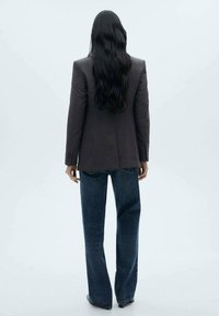 Mörkgrå kavaj med skräddarsydd passform, kombinerad med högmidjade, löst sittande blå jeans. Slät textur och rak silhuett.