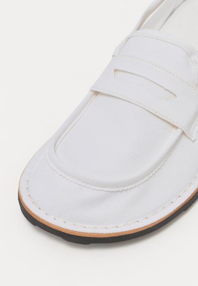 Hvide kanvas loafers med rund tå, featuring en frontrem og sort gummisål. Syningsdetaljer langs kanterne for ekstra tekstur.