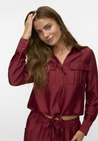 Burgundy satin shirt with a button-up design, structured collar, two front pockets, and shirred hem, paired with matching drawstring pants.
