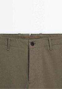 Pantalon marron sur mesure avec passants de ceinture et une fermeture à bouton noir unique à la taille.