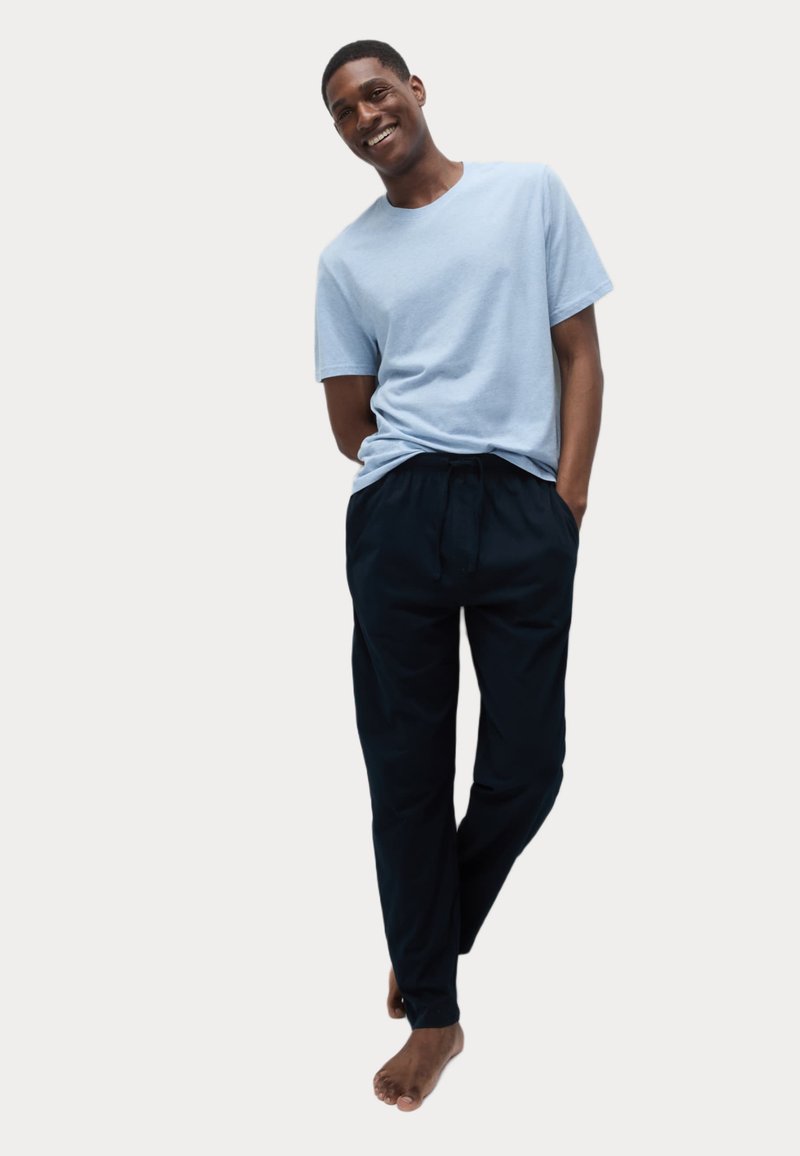 Camiseta de algodón azul claro combinada con pantalones negros de cordón. El conjunto tiene un corte holgado y se lleva descalzo, enfatizando la comodidad.